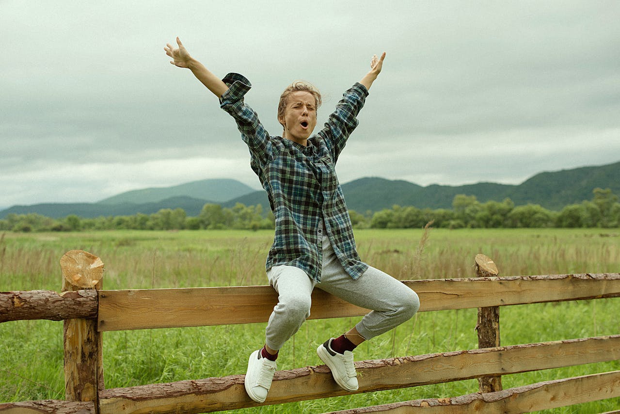 woman sitting on wooden fence with arms in the air